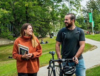 Une étudiante et un étudiant discutent et marchent ensemble avec un vélo