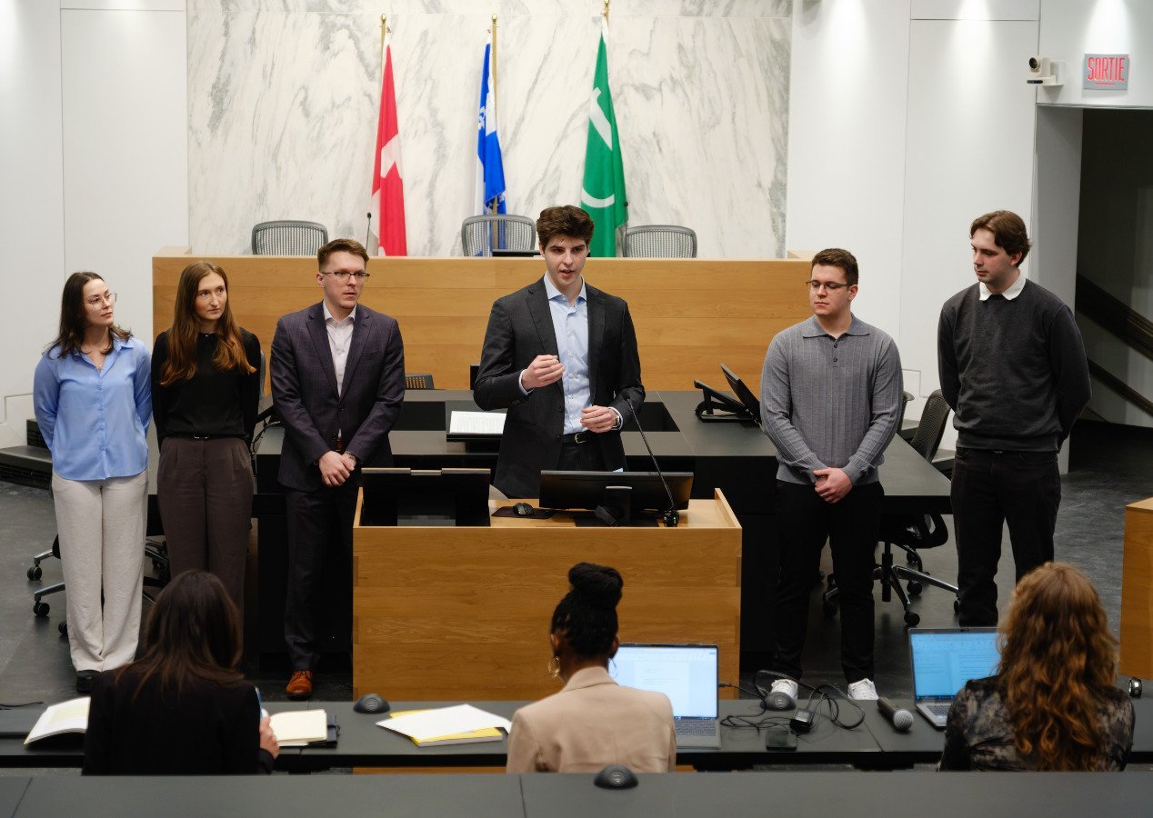 Deux étudiantes et quatre étudiants de droit faisant une présentation dans une salle d'audience.