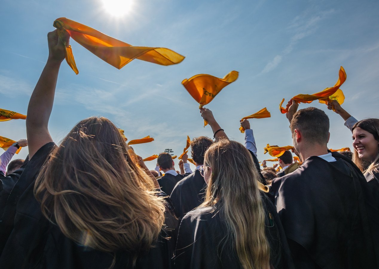Personnes diplômées en toge agitant un petit drapeau jaune