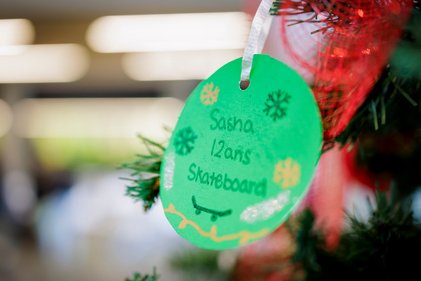 Boule de Noël en carton vert sur lequel figure le souhait d'une famille de tois enfants : recevoir une carte-cadeau d'un magasin à grande surface