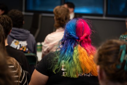 Une personne étudiante avec des cheveux aux couleurs de l'arc-en-ciel