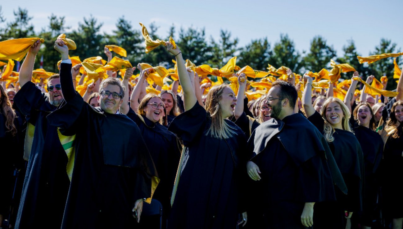Des dizaines de diplômés en toge noir et or, célébrant leur réussite en brandissant un foulard jaune