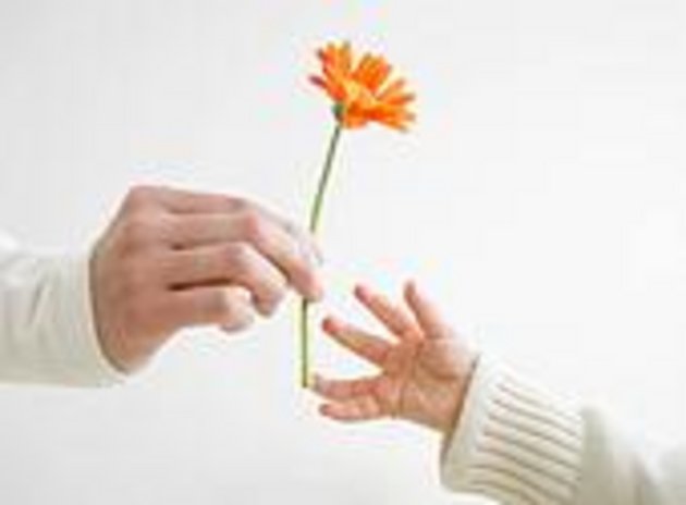 une main d'adulte qui donne une fleur orange à une main d'enfant 