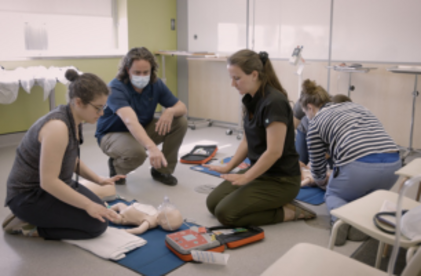 Instructeur qui donne des consignes aux participants qui vont réanimer un jeune mannequin de réanimation