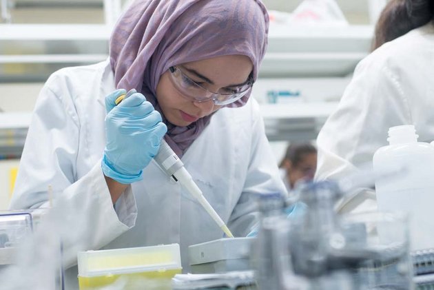 Femme voilée avec lunettes de protection, sarrau et gants travaille en laboratoire de biologie 