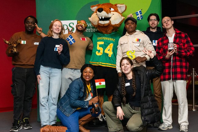 Des étudiantes et étudiants internationaux entourent Sherlo, la mascotte de l'UdeS.