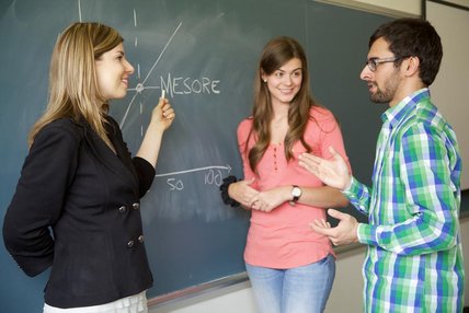 Deux femmes et un homme discutent devant notes sur tableau de classe