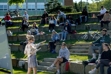 Une professeur enseigne en plein air devant des étudiants installés dans les gradins de pierre