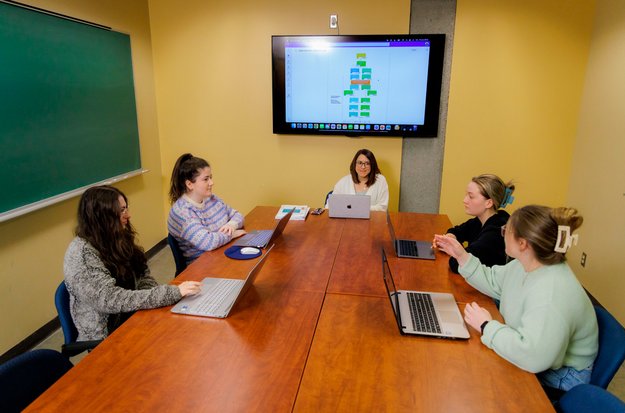 Cinq étudiantes en sciences infirmières, assises avec leurs portables autour d’une table, dans une salle de rencontre. 
