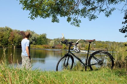 Un homme prend une pause pour admirer un étang, son vélo à proximité.