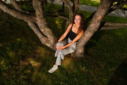 Emmy Ouellet, assise au creux d'un arbre, entourée de ses racines