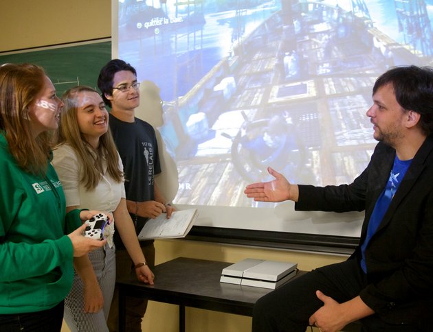 Un groupe d'étudiantes et étudiants en pleine discussion avec leur professeur, devant la projection d'une scène de jeu vidéo