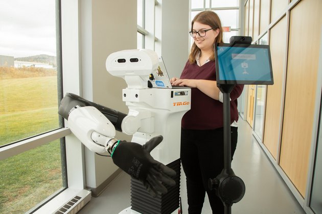 Étudiante travaillant avec un robot ayant une tête, un tronc et un bras avec main gantée