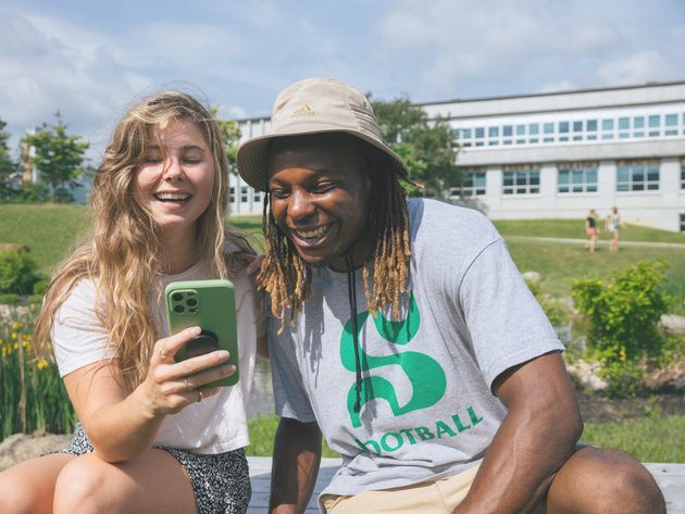 Une étudiante et un étudiant international rigolent en regardant un téléphone portable.