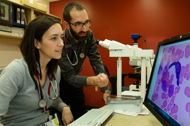 Photo of two specialists analyzing an image enlarged by a microscope.