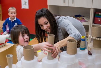 Fillette fabriquant un château de bols de plastique et de rouleaux de papier rigides avec son enseignante