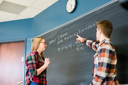 Deux étudiants qui s'entraident à résoudre un problème sur un tableau