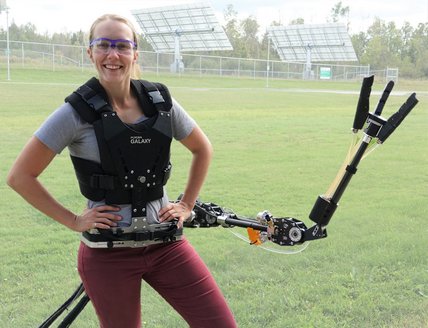Photo of a woman standing in a field with a robotic arm attached at her waist