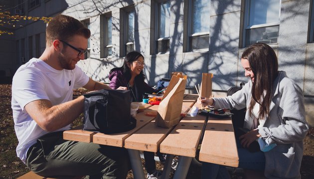 2 étudiantes et un étudiants mangent à l’extérieur de la faculté