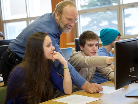 Professeur d'informatique montre du doigt l'écran d'un ordinateur à une étudiante et un étudiant