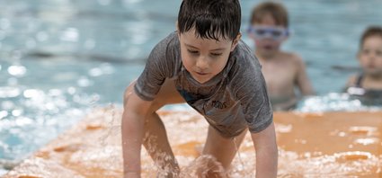 Un garçon grimpe sur un matelas flottant en piscine